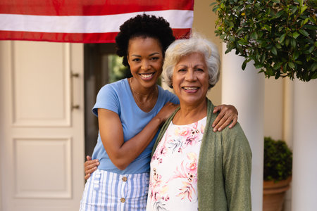 Portrait of smiling african american daughter with arm around mother at house entrance. family and bonding, unaltered.の写真素材