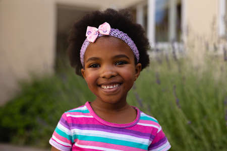 Portrait of smiling cute african american girl wearing headband and striped t-shirt. childhood and...