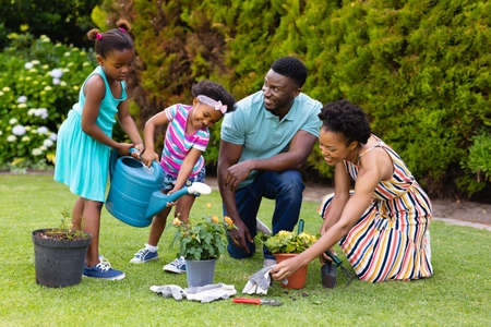 Happy african american family watering plants together in garden. family, love and togetherness concept, unaltered.の写真素材