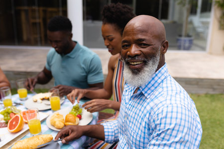 Portrait of smiling bearded bald african american senior man eating brunch with family at backyard. family, love and togetherness concept, unaltered.の写真素材