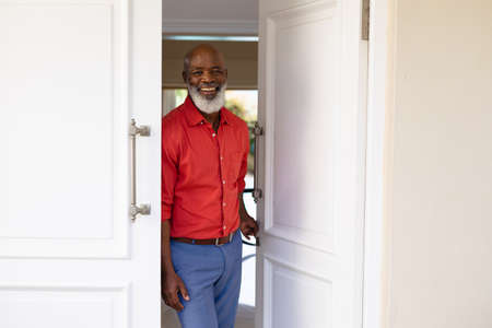 Portrait of bearded african american senior man smiling while standing at the front door of house. people and home concept, unaltered.の写真素材