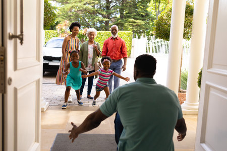African american girls running towards their father on the front door at home. family, love and togetherness concept, unaltered.の写真素材