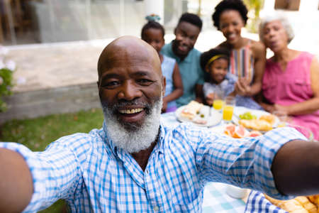 Portrait of smiling bearded bald senior african american man taking selfie with family at brunch. family, love and togetherness concept, unaltered.の写真素材