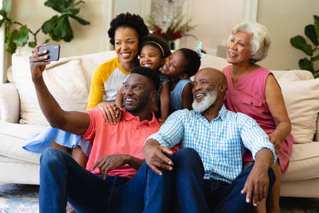 Smiling african american three generation family taking a selfie sitting together on couch at home. family, love and togetherness concept, unaltered.の写真素材