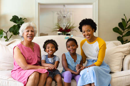 Portrait of african american grandmother, mother and two granddaughters smiling sitting on couch. family, love and togetherness concept, unaltered.の写真素材