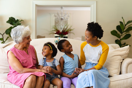 African american grandmother, mother and two granddaughters smiling looking at each other at home. family, love and togetherness concept, unaltered.の写真素材