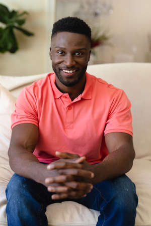 Portrait of african american man smiling while sitting on the couch at home. people and emotions concept, unaltered.の写真素材