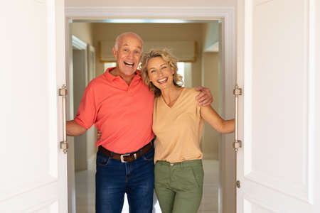 Portrait of caucasian senior couple smiling while opening the front door of house. home welcome...
