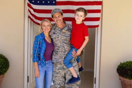 Portrait of caucasian military man with woman and carrying son standing at house entrance. family, love and patriotism concept, unaltered.の写真素材