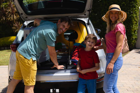 Portrait of caucasian family putting their luggage in their car on sunny day. family trip and...