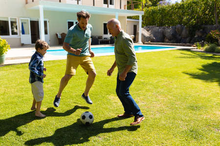 Caucasian grandfather, father and son playing football together in the garden. family, sport and...