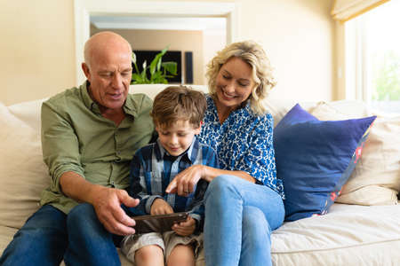 Caucasian grandparents and grandson using digital tablet while sitting together on the couch at...