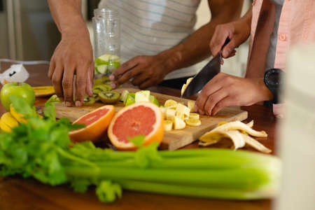 Midsection of young african american couple cutting fresh fruits on board in kitchen. people, love...