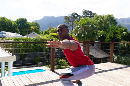 Active african american man practicing yoga at terrace on sunny day. people and healthy lifestyle concept, unaltered.の写真素材
