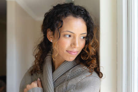Beautiful young biracial woman wearing sweater looking away at home. people and emotions concept,...
