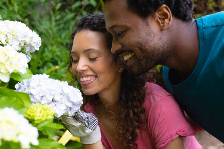 Smiling young biracial couple smelling fresh bunch of flowers in backyard garden. people, nature and togetherness concept, unaltered.の写真素材