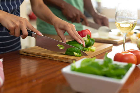 Midsection of young biracial woman cutting bell pepper in kitchen at home. people and cooking concept, unaltered.の写真素材