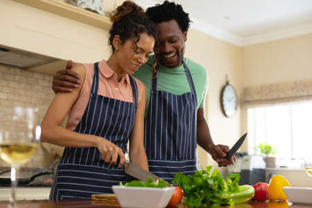 Happy young multiracial couple cooking meal together at kitchen island. people, togetherness and...