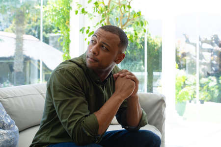 Thoughtful young african american man sitting with hands clasped while looking over shoulder at...