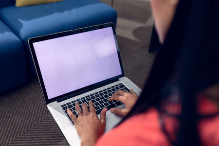 Midsection of biracial young businesswoman using laptop with blank screen working in office. unaltered, creative business, copy space, modern office and wireless technology concept.の写真素材