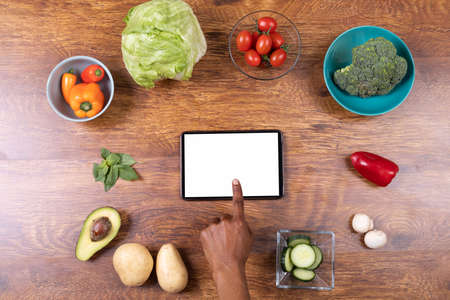 Directly above shot of cropped hand using tablet pc amidst various food on table, copy space. unaltered, food, wireless technology, fitness and healthy eating concept.の写真素材
