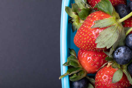 Overhead view of fresh strawberries and blueberries in tiffin over black background, copy space. unaltered, food and healthy eating concept.の写真素材