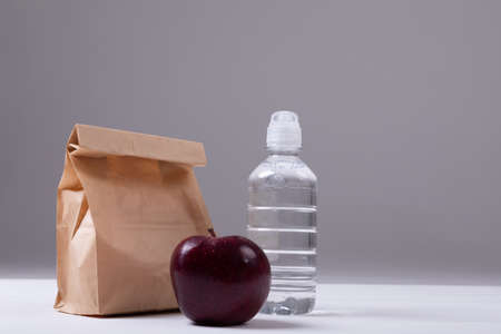 Close-up of apple and paper lunch bag with water bottle on table against gray background. unaltered, healthy food, copy space, fruit, drink and packed lunch.の写真素材