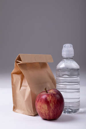 Close-up of brown paper lunch bag with apple and water bottle on table against gray background. unaltered, healthy food, copy space, fruit, drink and packed lunch.の写真素材