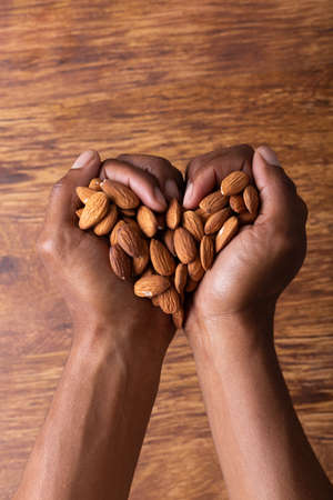 Directly above shot of cropped hands holding almonds in heart shape over wooden table. unaltered, healthy food, copy space, snack, organic, nut, hands cupped, lifestyle and dried food.の写真素材