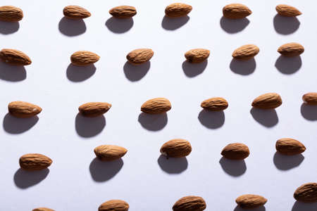 Full frame shot of almonds arranged side by side on white background with copy space. unaltered, healthy food, snack, copy space, organic, shadow, light, nut and dried food.の写真素材