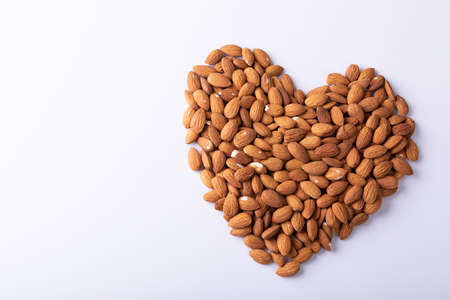 High angle close-up of almonds arranged in heart shape pattern on wooden white background. unaltered, healthy food, snack, organic, nut and dried food.の写真素材