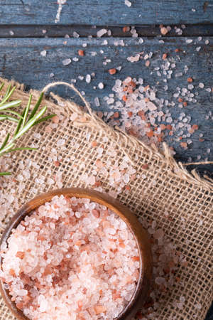 Close-up of himalayan pink rock salt in wooden bowl with rosemary on jute fabric over table. unaltered, ingredient, food, rock salt, herb and seasoning.の写真素材