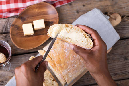Cropped hands of african american man applying butter on bread slice. unaltered, healthy food, slice, lifestyle and baked food.の写真素材