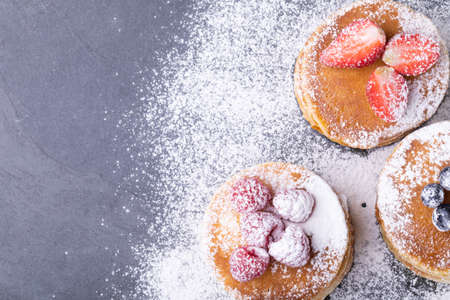 Overhead view of powdered sugar over stacked pancakes with various berry fruits on food slate. unaltered, breakfast, sweet food, organic and healthy food concept.の写真素材