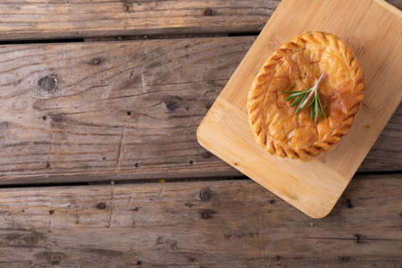 Directly above shot of baked stuffed pie with rosemary on wooden serving board at table. unaltered,...