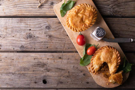 Directly above shot of stuffed pies with tomatoes, herbs and salt shaker on serving board at table. unaltered, baked, wood, sliced and healthy food concept.の写真素材