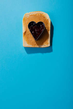 Close-up of jam in heart shape pastry cutter over bread with peanut butter on blue background....