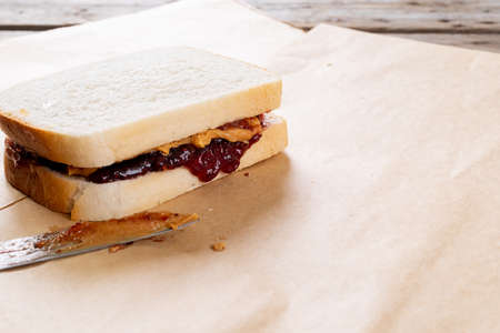 Close-up of peanut butter and jelly sandwich on brown paper with table knife at table. unaltered, peanut butter and jelly sandwich, healthy food and breakfast.の写真素材