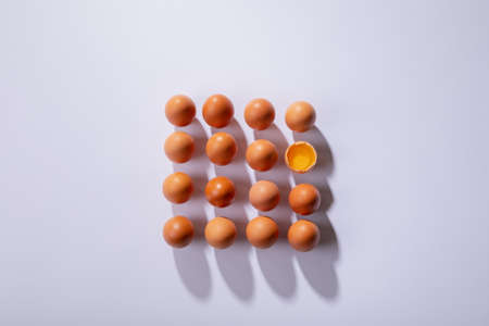 Overhead view of brown eggs with one broken egg arranged in square on table. unaltered, healthy food, raw food, organic, protein, fresh, egg yolk, shadow and still life.の写真素材