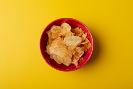 Overhead view of potato chips in red bowl on yellow background. unaltered, unhealthy food, snack and salty snack.の写真素材