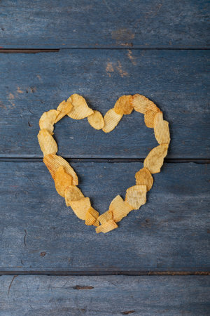 Overhead view of potato chips arranged in heart shape on wooden table. unaltered, unhealthy food,...