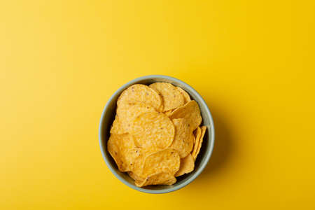 Directly above shot of chips in bowl on yellow background with copy space. unaltered, unhealthy food, snack and crunchy snack.の写真素材