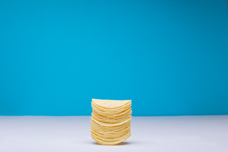 Stack of potato chips on table against blue background with copy space. unaltered, unhealthy food, snack, copy space and salty snack.の写真素材