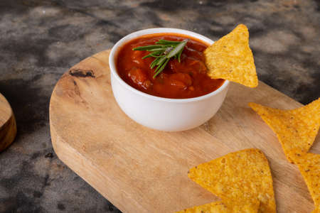 Close-up of nacho chips and red sauce with rosemary herb served on serving board at table....