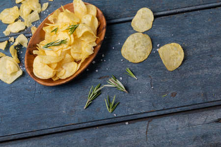 High angle view of potato chips in bowl with rosemary and salt on wooden table. unaltered, unhealthy food, snack, herb and salty snack.の写真素材