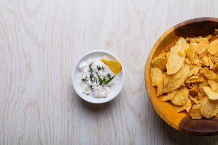Overhead view of white dipping sauce with herbs served by potato chips in bowl on table. unaltered, unhealthy food, snack, dipping sauce, herb, crunchy, salty snack and savory food.の写真素材