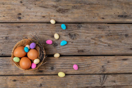 Directly above shot easter eggs and colorful candies in nest on wooden table. unaltered, cultures,...