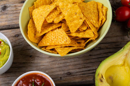 Close-up of nacho chips in bowl with dips and vegetables on table. unaltered, unhealthy food, snack, dipping sauce, crunchy and savory food.の写真素材
