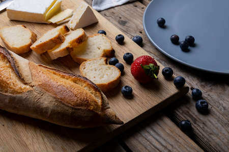 Close-up of sliced baguette with blueberries, strawberry and cheese on serving board at table. unaltered, healthy food, french food, berry fruit and baked food.の写真素材