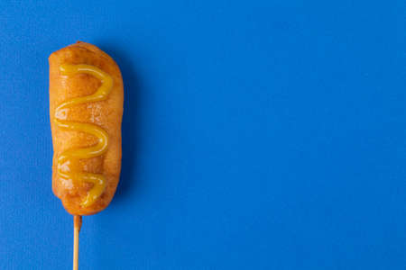 Overhead view of corn dog with mustered sauce over skewer on blue background with copy space. unaltered, copy space, unhealthy food, meat, sausage and fried food.の写真素材